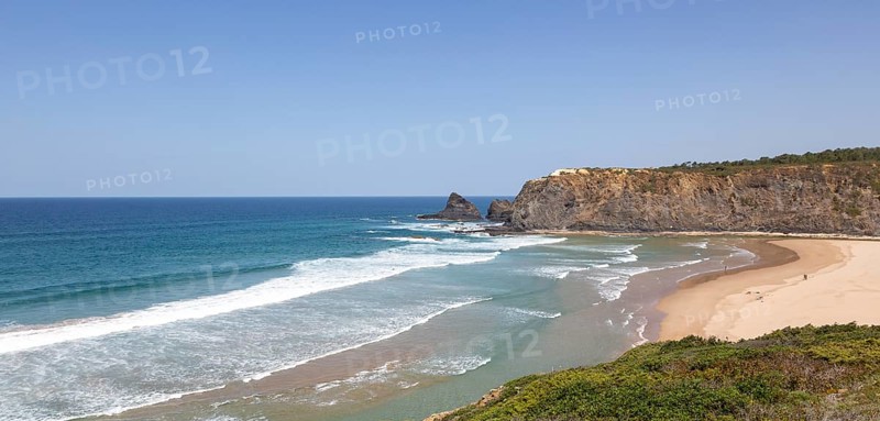 Atlantic Ocean waves breaking on rocky headland and bay with wide sandy beach, surfer and a few sunbathers, Praia de Odeceixe, Algarve, Portugal, Southern Europe, Europe
