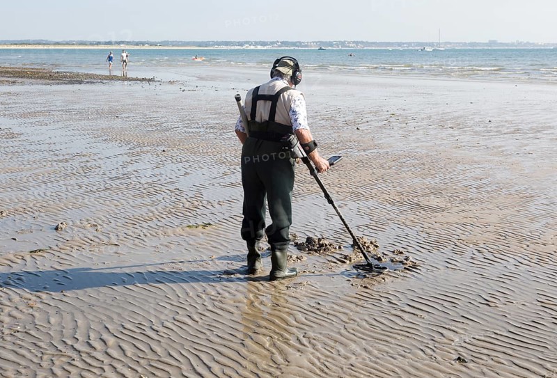 Male detectorist using metal detector at low tide, sandy beach Studland Bay, Swanage, Dorset, England, UK