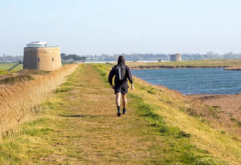 Man walking coastal path on sea wall dyke at Bawdsey, Suffolk, England, UK