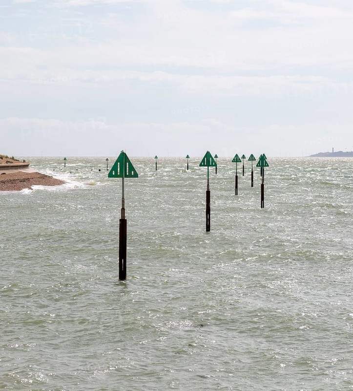 Green triangular warning markers on posts in shallow water at River Orwell river mouth, Landguard Point, Felixstowe, Suffolk, England, UK