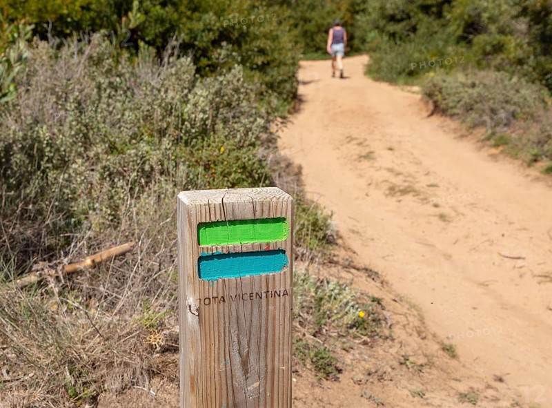 One woman walking in woodland on coastal long distance footpath trail, The Fisherman's Walk or Ruta Vicentina, near Zambujeira do Mar, Alentejo Littoral, Portugal, Southern Europe. In the foreground is the painted way mark sign for the route, Europe