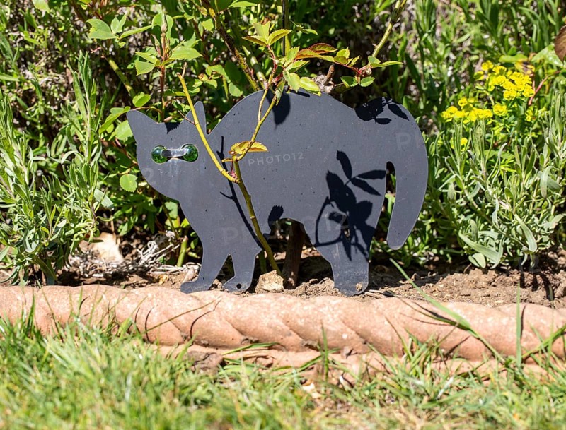 Black metal cat scarer in garden with green glass eyes to deter cats, UK