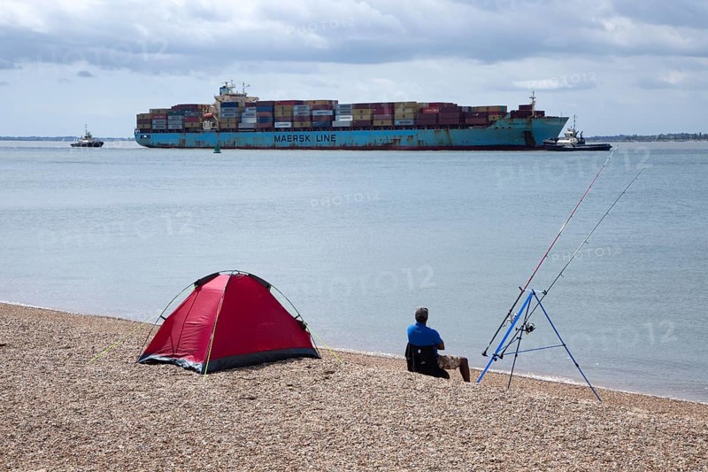 Fisherman watches arrival of Maersk Utah container ship at Port of Felixstowe, Suffolk, England, UK