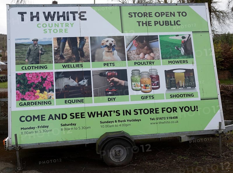 Mobile wheeled advertising hoarding for TH White country store shop, Marlborough, Wiltshire, England, UK