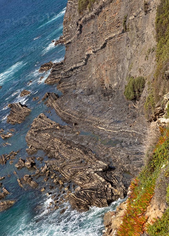 Intensely folded rock of wave cut platform at the base of a steep cliff. Rocky rugged coastal landscape on the Rota Vicentina Fisherman's Trail long distance footpath route, near Bunheira, Aljezur, Algarve, Portugal, Southern Europe, Europe