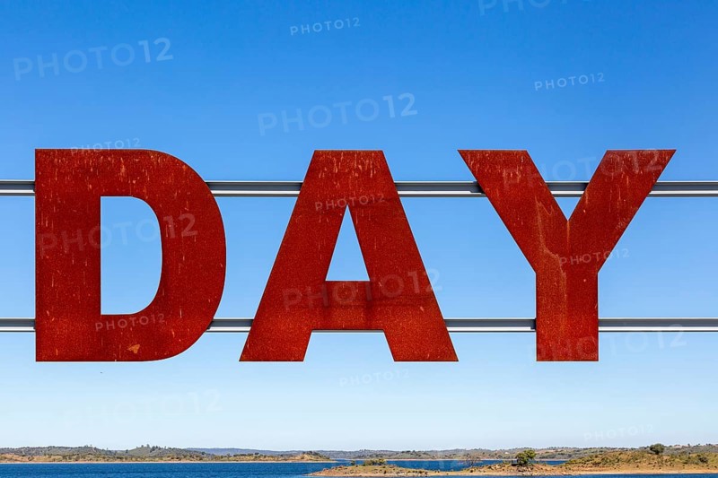 Large red rusty capital letters spell the word DAY against blue sky background, Alqueva dam, Moura, Portugal, Europe