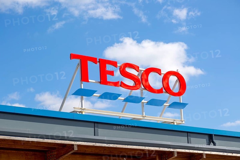 Bright red Tesco store sign against blue sky and white fluffy cumulus clouds