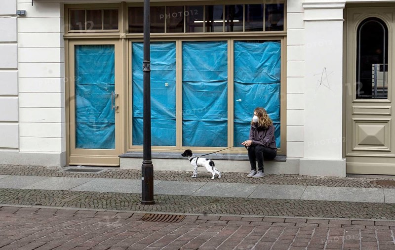 A woman sits with her dog in front of a closed shop. Customers who want to buy in retail stores in the city must present a negative corona test, Potsdam, 27.03.2021