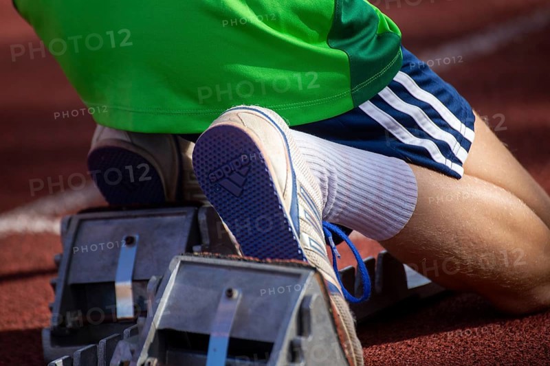 Young track and field athlete with Adidas spikes at the starting block in front of a sprint