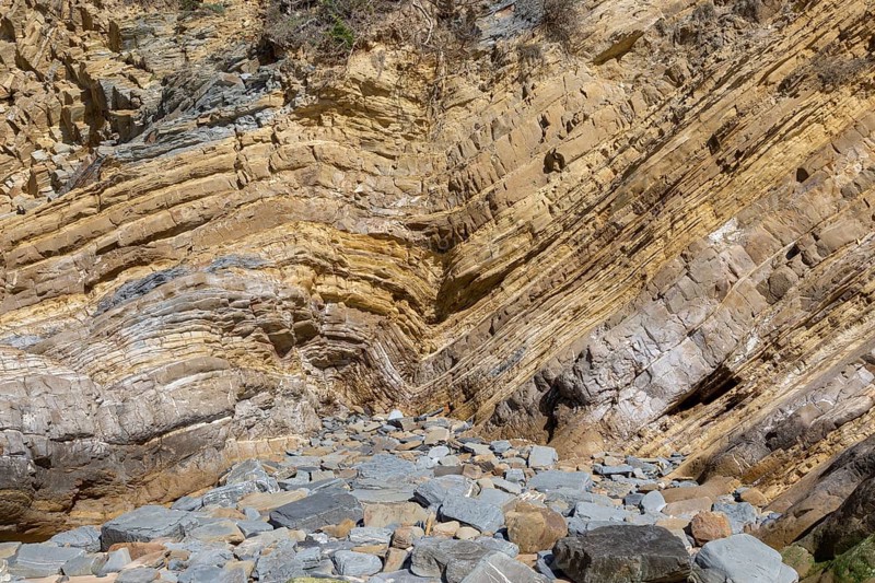 Strata of sandstone sedimentary rock in a coastal cliff with layers folded down to form a geological structure called a syncline, near Zambujeiro do Mar, Alentejo Littoral, Portugal, southern Europe. A syncline is a trough or fold of stratified rock in which the strata slope upwards from the axis. Folds typically form during crustal deformation as the result of compression that accompanies orogenic mountain building, Europe