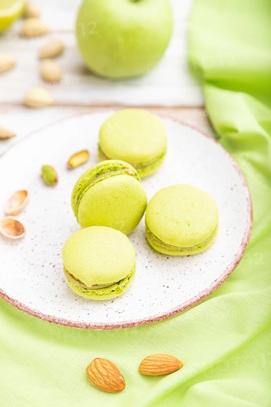 Green macarons or macaroons cakes with cup of coffee on a white wooden background and green linen textile. Side view, close up, selective focus