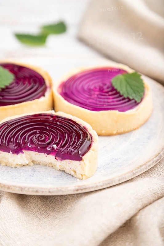 Sweet tartlets with jelly and milk cream with cup of coffee on a white wooden background and linen textile. Side view, close up, selective focus