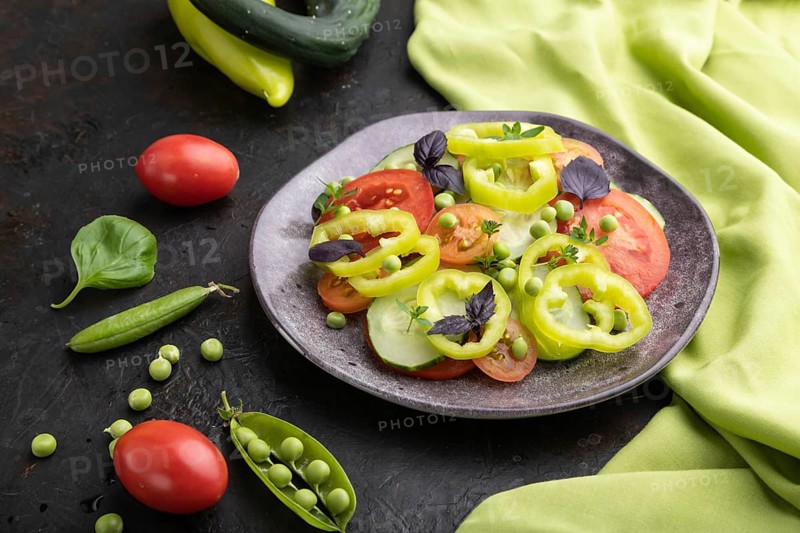 Vegetarian salad from green pea, tomatoes, pepper and basil on a black concrete background and green textile. Side view, close up