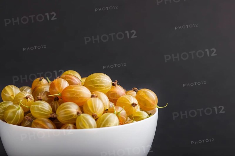 Fresh green gooseberry in white bowl on black background. side view, copy space, close up, selective focus