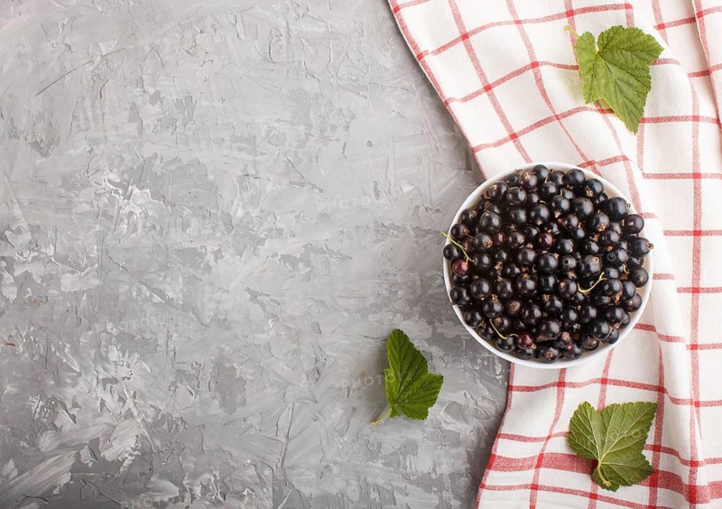 Fresh black currant in white bowl and linen textile on gray concrete background. top view, copy space