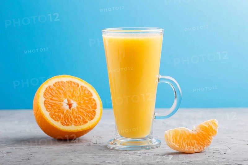 Glass of orange juice on a gray and blue background. Morninig, spring, healthy drink concept. Side view, close up