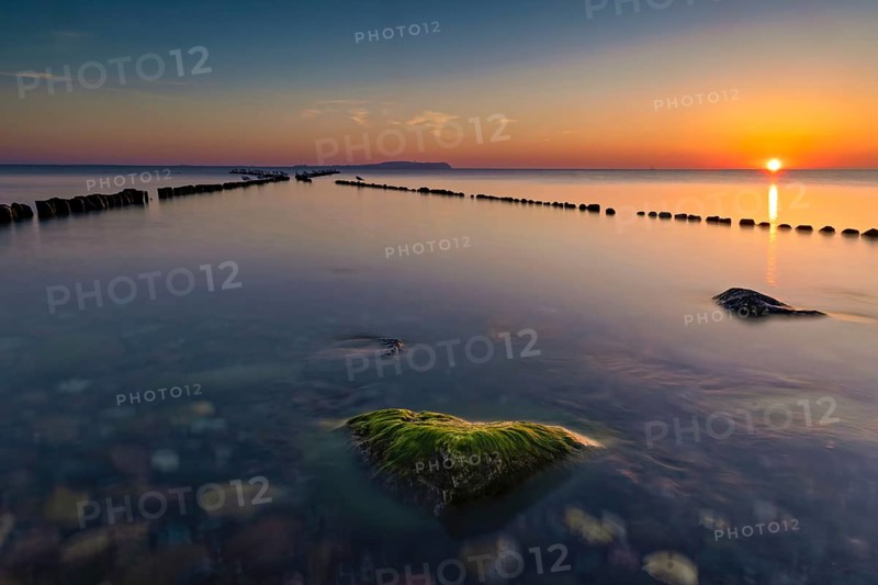 Sunset at the double stage in Dranske on the island of Ruegen. A green stone overgrown with algae provides a beautiful eye-catcher