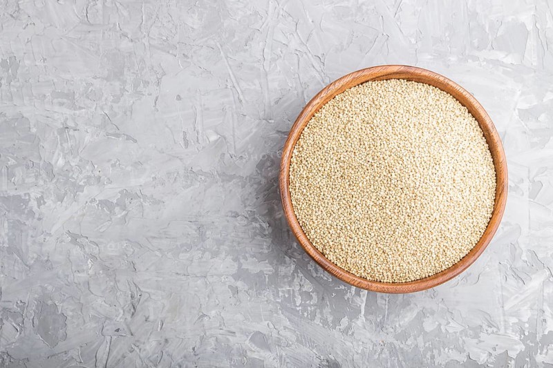 Wooden bowl with raw white quinoa seeds on a gray concrete background. Top view, flat lay, copy space