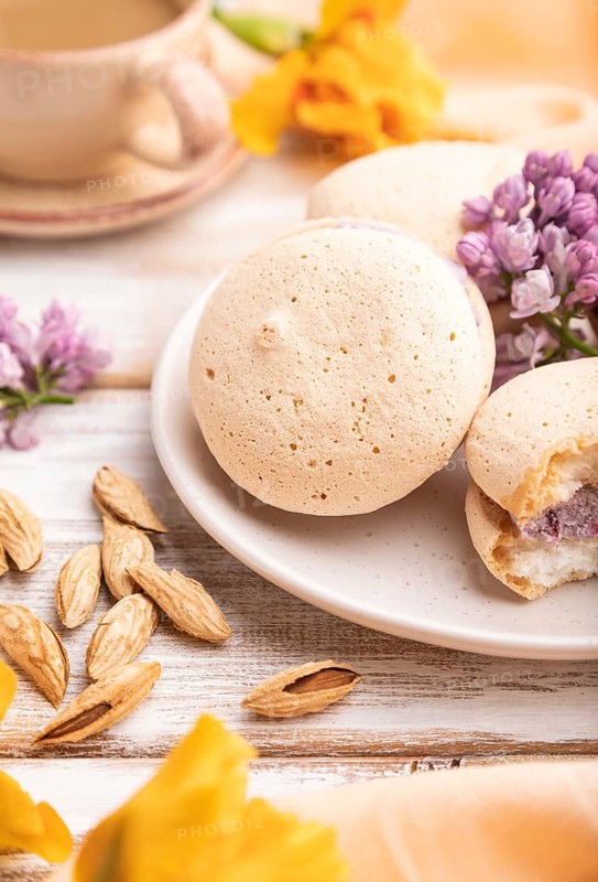 Meringues cakes with cup of coffee on a white wooden background and orange linen textile. Side view, close up, selective focus