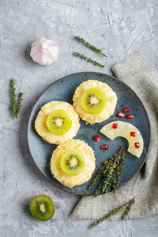 Pieces of baked pork with pineapple, cheese and kiwi on gray background, top view