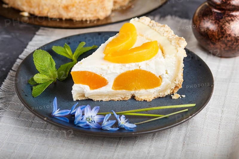 A piece of peach cheesecake on a blue ceramic plate with blue flowers and a cup of coffee on a linen napkin on a black concrete background. side view, close up, selective focus