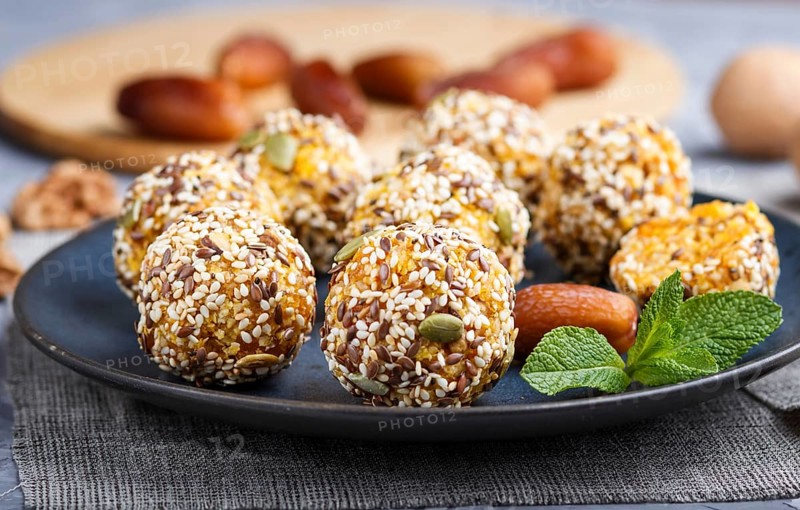 Energy ball cakes with dried apricots, sesame, linen, walnuts and dates with green mint leaves on a blue ceramic plate. side view, close up, macro, selective focus. vegan homemade candy