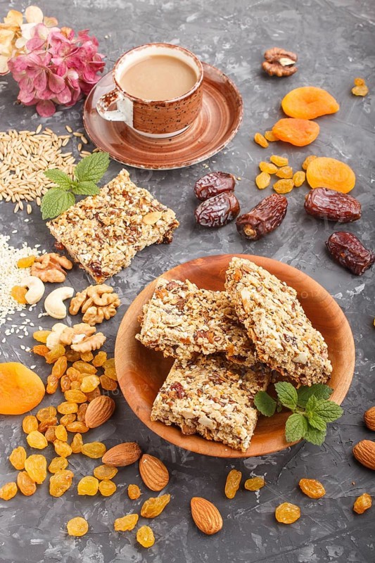 Homemade granola from oat flakes, dates, dried apricots, raisins, nuts with a cup of coffee on a black concrete background. Side view, close up