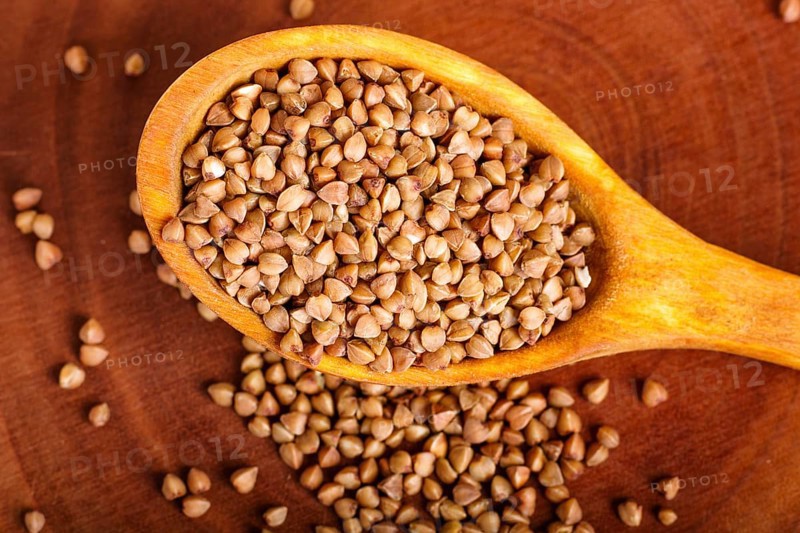 Pile of buckwheat in a wooden spoon on brown background. Closeup