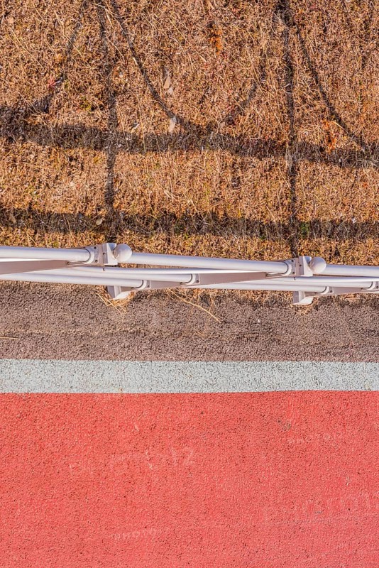 Looking down onto red bike path next to metal guardrail casting its shadow on brown grassy area in South Korea