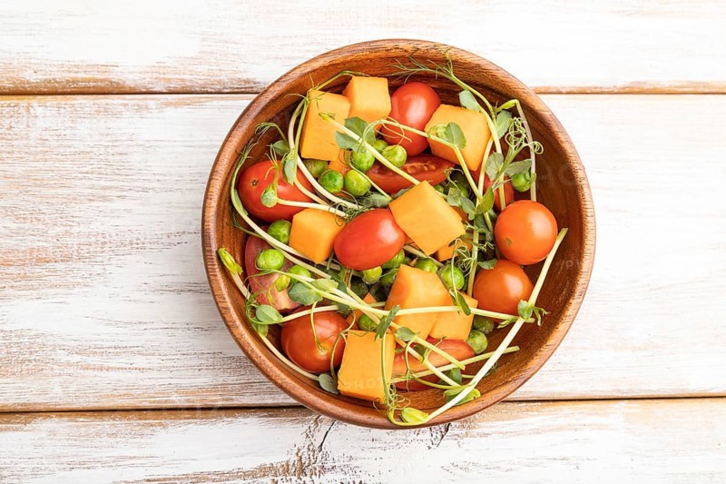 Vegetarian vegetable salad of tomatoes, pumpkin, microgreen pea sprouts on white wooden background. Top view, flat lay, copy space