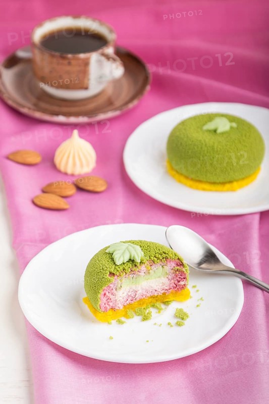 Green mousse cake with pistachio and strawberry cream on a white wooden background and pink textile. side view, close up, selective focus