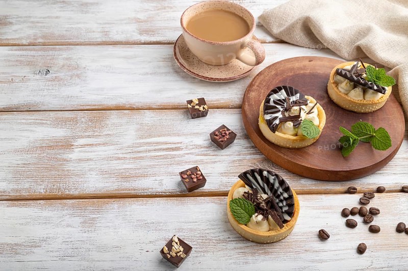 Sweet tartlets with chocolate and cheese cream with cup of coffee on a white wooden background and linen textile. side view, copy space