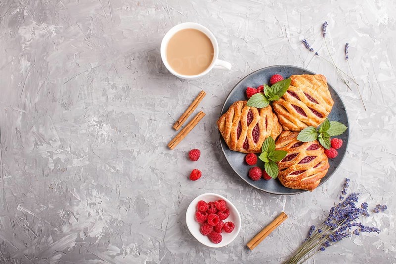 Puff pastry buns with strawberry jam on blue ceramic plate on gray concrete background, cup of coffee, lavender, cinnamon, mint leaves. top view, flat lay, copy space