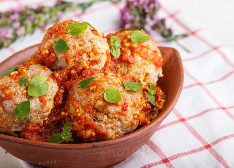 Pork meatballs with tomato sauce, oregano leaves, spices and herbs in clay bowl on a white wooden background with linen textile. side view, close up, selective focus