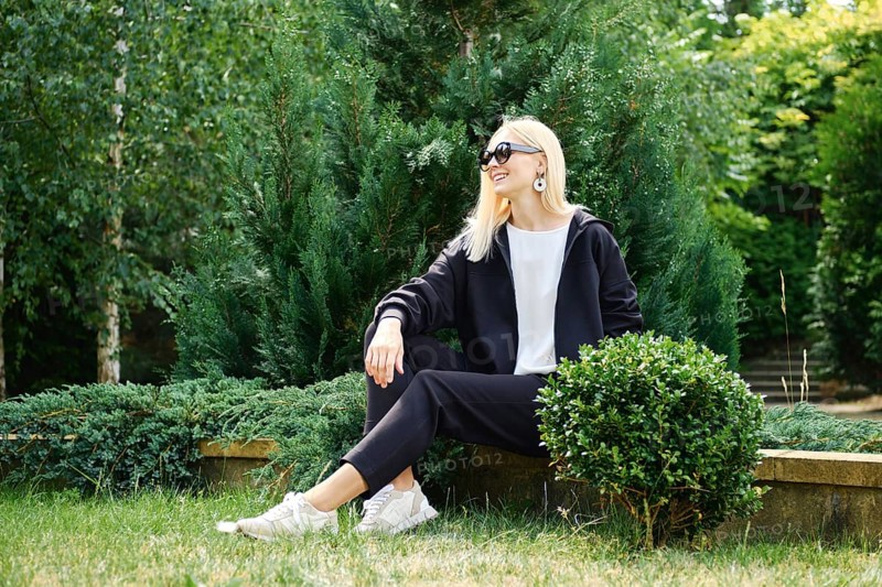 Woman in black hoodie and fleece trousers rests on backyard