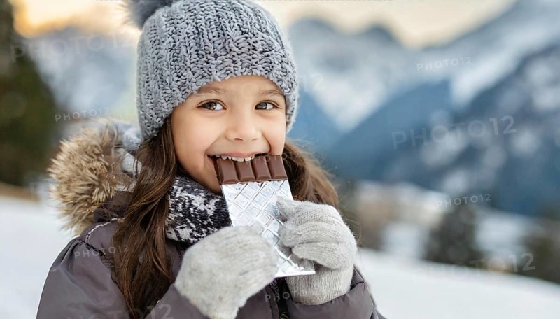 KI generated, Young girl, 10, years, eating a bar of chocolate, one person, outdoor shot, ice, snow, winter, seasons, eating, eating, hat, bobble hat, gloves, winter jacket, cold, coldness