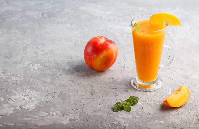 Glass of peach juice on a gray concrete background. Morninig, spring, healthy drink concept. Side view, copy space