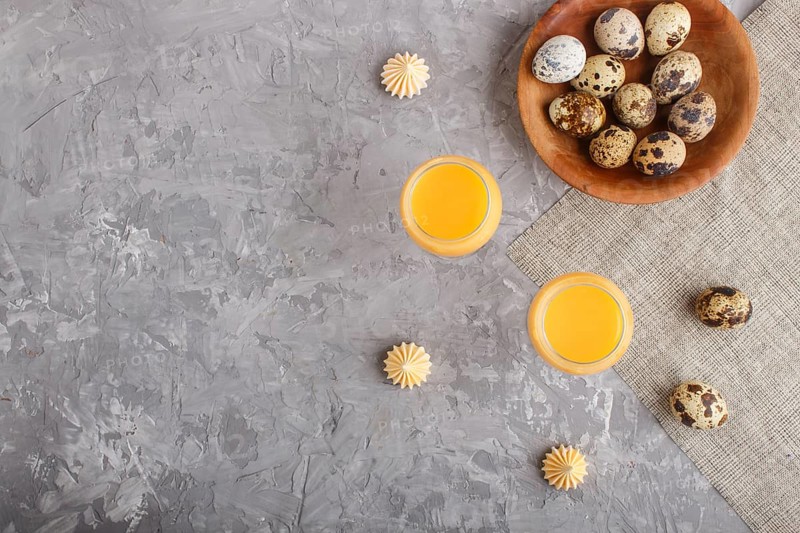 Sweet egg liqueur in glass with quail eggs and meringues on a gray concrete background. Top view, copy space, flat lay