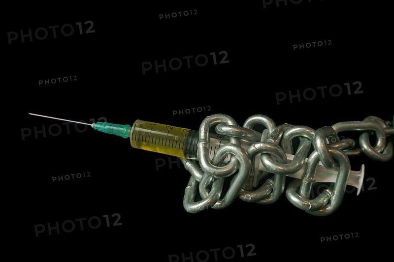 Syringe filled with yellow liquid tied with a chain isolated on black background and copy space, addiction concept