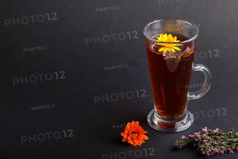 Glass of herbal tea with calendula and hyssop on a black background. Morninig, spring, healthy drink concept. Side view, copy space