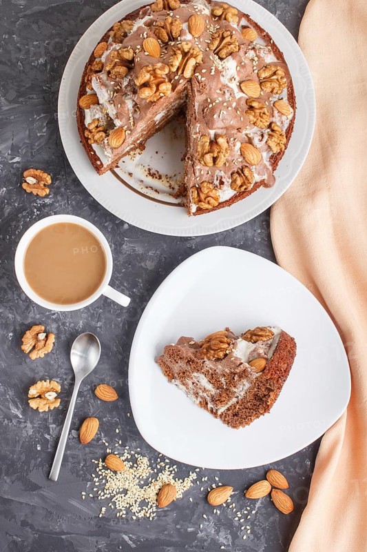 Homemade cake with milk cream, cocoa, almond, hazelnut on a black concrete background with orange textile and a cup of coffee. Top view, flat lay, close up