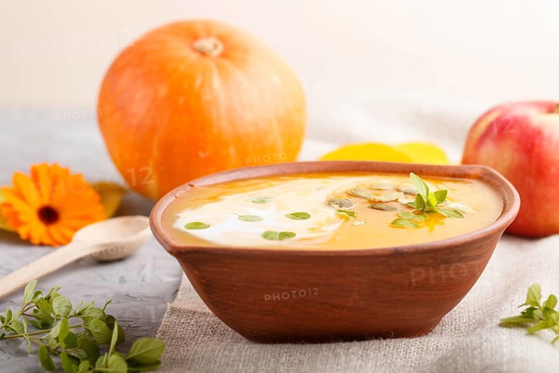 Traditional pumpkin cream soup with seeds in clay bowl on a gray concrete background with linen textile. side view, close up, selective focus