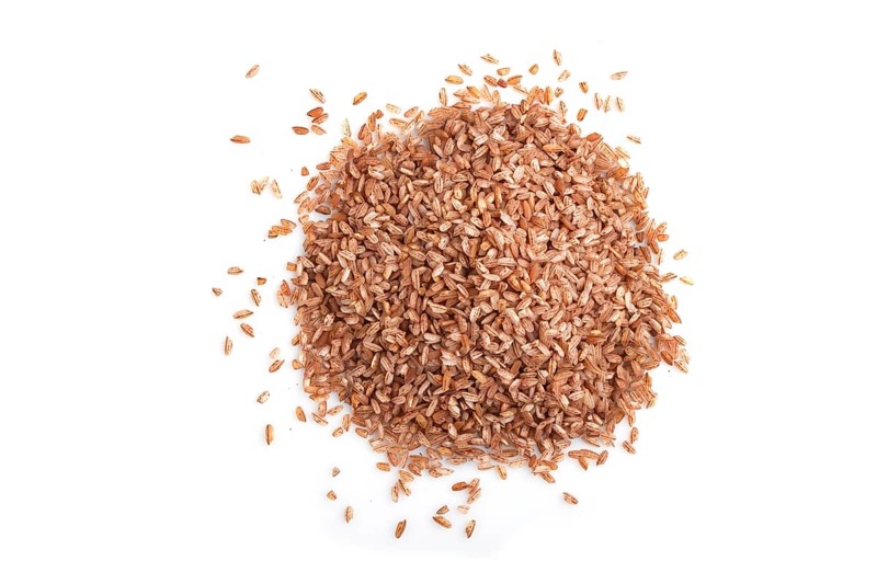 Heap of unpolished brown rice isolated on white background. Top view, flat lay, close up, macro