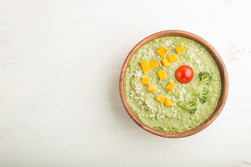 Green broccoli cream soup in wooden bowl on a white wooden background. top view, flat lay, copy space