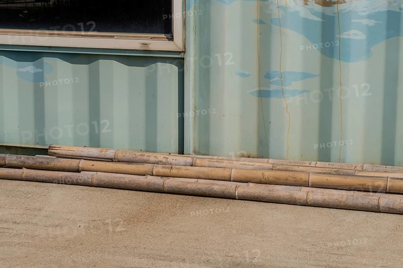 Weathered cracked bamboo poles laying on concrete driveway in front of aluminum building wall in South Korea