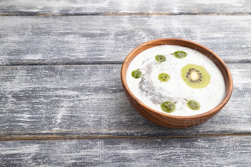 Yogurt with kiwi, gooseberry, chia and almonds in wooden bowl on gray wooden background. side view, copy space, close up