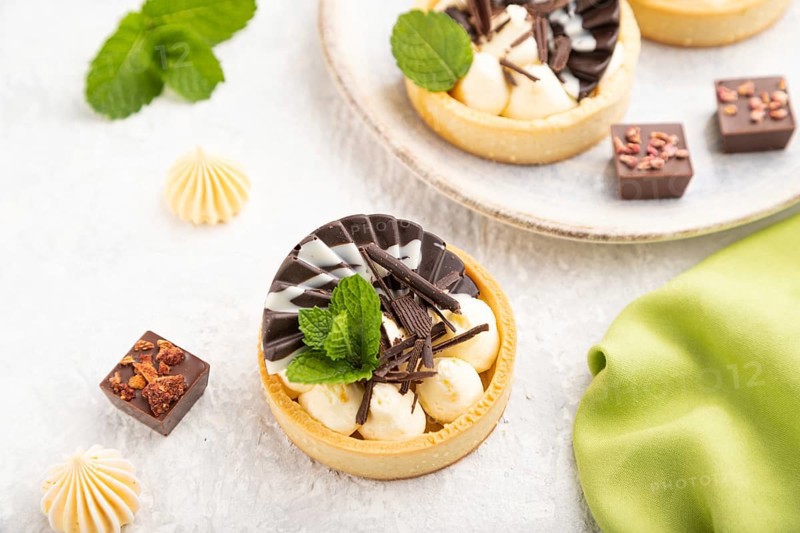 Sweet tartlets with chocolate and cheese cream with cup of coffee on a gray concrete background and green textile. Side view, close up, selective focus