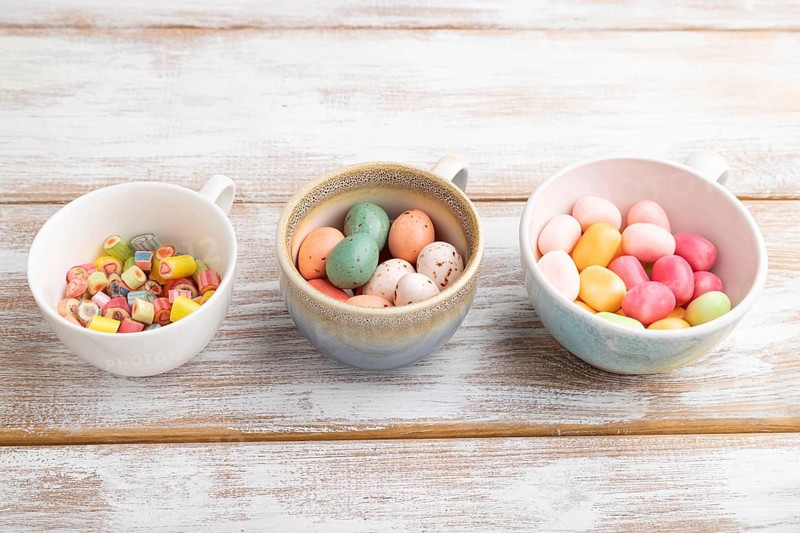 Heap of multicolored caramel candies in cups on white wooden background. copy space, side view, close up