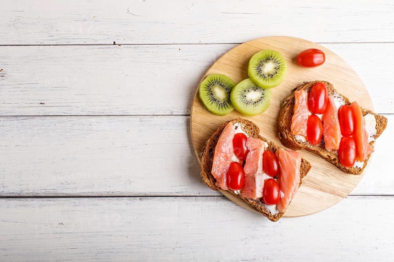 Smoked salmon sandwiches with butter and cherry tomatoes on white wooden background. top view, copy space
