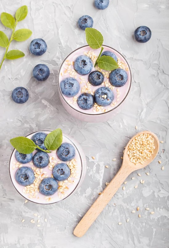 Yoghurt with blueberry and sesame in a glass and wooden spoon on gray concrete background. top view, flat lay, close up